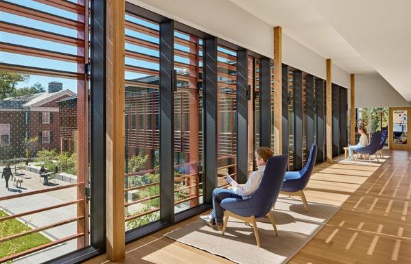 People sitting in a sunny hallway looking out over the Living Village plaza at Yale Divinity School