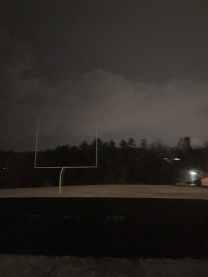 In the middle of the track is the practice field. Visible against the darkness is the yellow uprights of an American football goal post. The grass, of the warm weather variety, is brown and dormant. 