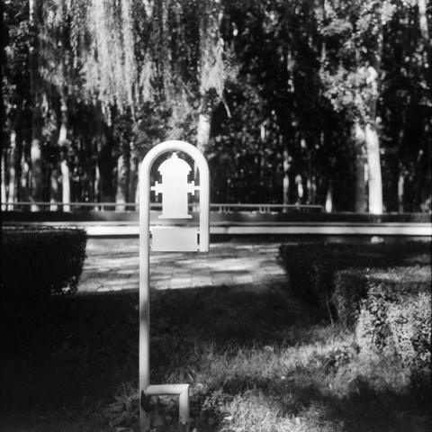 Lucky SHD 400 (6x6)

English:
This black-and-white image features a close-up of a white fire hydrant sign, which is shaped like a hydrant with an arch above it. The sign is positioned in front of a row of trees, creating a sense of depth. The trees are tall and slender, with their trunks and branches forming a rhythmic pattern. The background includes a paved path and neatly trimmed bushes, adding to the orderly and serene atmosphere of the scene.
Chinese (中文):
这张黑白照片特写了一块白色消防栓标志，标志形状像消防栓，上方有拱形…
