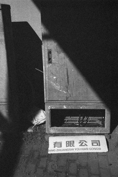 Ilford HP5 Plus 400 (FF)

English Alt Text: A black-and-white urban photo shows a metal utility cabinet against a wall. The cabinet has a rectangular opening at the bottom, revealing wires or internal components. In front of it lies a sign with Chinese characters and Romanized text reading “JIANG ZHUANGSHI YOUXIAN GONGSI.” The ground is paved with bricks and littered with debris. Shadows partially cover the scene, adding dramatic contrast.

中文替代文字： 这是一张黑白城市照片，画面中一个金属电箱靠墙而立，底部有一个矩形开口，露出内部电线或部件。电…