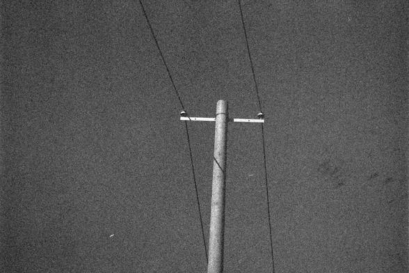 Ilford HP5 Plus 400 (FF)

English Alt Text: A minimalist black-and-white photograph features a utility pole with two diagonal power lines extending upward. The pole has a horizontal crossarm with insulators attached. The background is a grainy sky, possibly due to film texture. The composition is simple and stark, evoking a vintage or artistic mood.

中文替代文字： 这是一张极简风格的黑白照片，画面中是一根电线杆，两条电线从两侧斜向上延伸。电线杆顶部有一根横杆，安装着绝缘器。背景是颗粒感强烈的天空，可能是胶片质感造成的。构图简洁，风格冷峻，营造出复古或艺术氛围。
