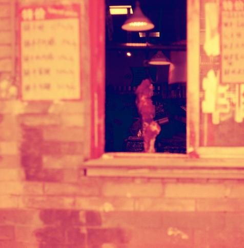 Harman Red 125 (6x6)

English Alt Text:
A storefront window of a traditional meat shop. A large piece of meat hangs inside, visible through the glass. Two warm-toned hanging lamps illuminate the interior, where shelves with various items are faintly seen. The window is framed in red, and the exterior wall is made of brick. The image is bathed in a reddish-orange hue, creating a nostalgic and atmospheric mood. Chinese signs flank the window but are blurred.
中文替代文字：
这是一家传统肉铺的橱窗图像。玻璃窗内挂着一块大肉，店内有两盏…