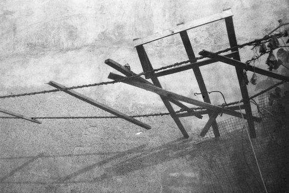 ERA 100 (FF)

English Alt Text:
A black-and-white photograph of a broken wooden structure made of intersecting beams, barbed wire, and mesh fencing. The background is a rough concrete wall, and dried vines hang from the right side. The composition evokes themes of decay, resilience, and contrast between nature and human-made elements.
中文替代文字：
一张黑白照片，画面是一座由木梁、铁丝网和铁丝构成的破旧结构，梁木交错排列。背景是一面粗糙的混凝土墙，右侧垂挂着干枯的藤蔓。整体构图传达出衰败与坚韧的主题，以及自然与人造元素之间的对比。