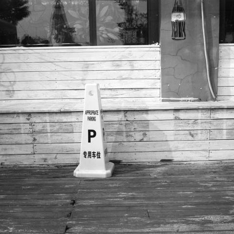 Lucky SHD 400 (6x6)

English Alt Text:
A black and white photo of a single traffic cone placed on a wooden deck in front of a building. The cone is labeled with English and Chinese text reading “APPROPRIATE PARKING P 专用车位,” indicating a designated parking space. The background includes a concrete and wood-paneled wall, a window reflecting light, and a hanging lamp. The composition emphasizes contrast and texture, with the cone standing out against the muted tones of the deck and building.
中文替代文…
