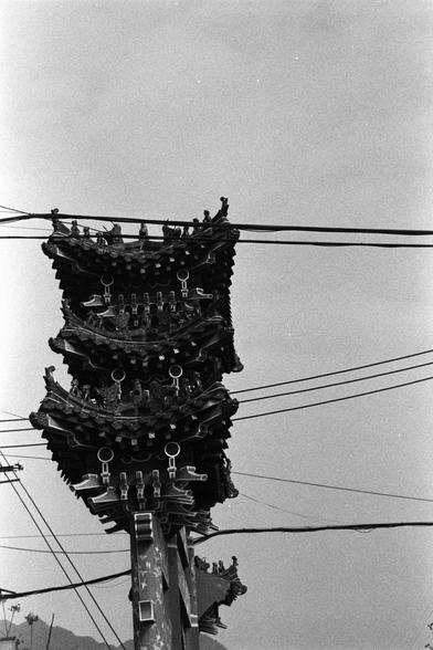 NEOPAN SS 100 (FF)

English Alt Text:
A black-and-white photo of a traditional Chinese archway with multiple ornate tiers of eaves. Each tier features intricate carvings and small figurines, typical of classical Chinese architecture. The structure is intersected by a web of overhead utility wires, creating a stark contrast between ancient design and modern infrastructure. The image evokes a sense of cultural heritage disrupted by urban development.
中文替代文字：
这是一张黑白照片，展示了一座传统的中国牌楼建筑。牌楼有多层飞檐，每层都雕刻着…
