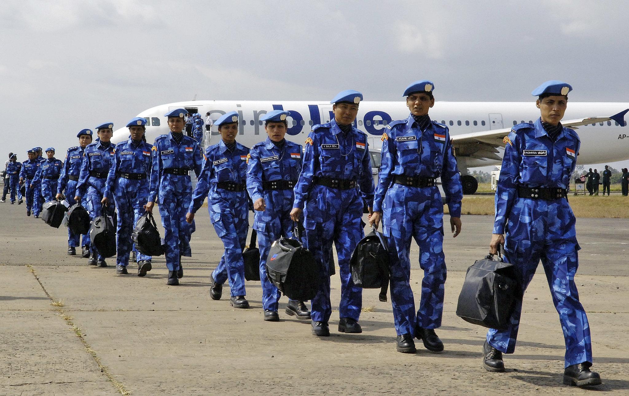 A line of women in blue camouflage uniforms and blue berets disembarking at an airport.