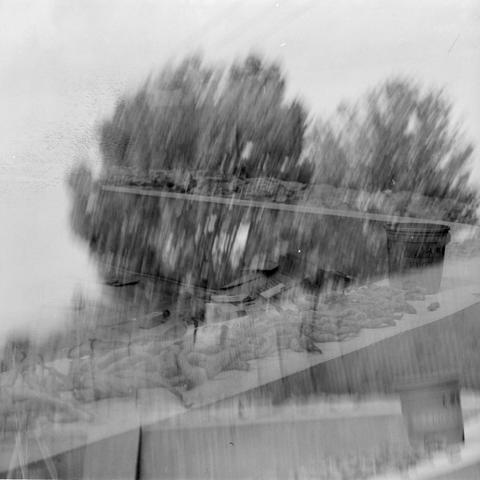 Lucky SHD 400 (6x6)

English Alt Text:
An abstract black-and-white double exposure photograph blending two scenes. The first layer shows trees reflected in calm water, evoking a peaceful natural setting. The second layer overlays a tabletop with various objects, possibly food items or small tools, and a bucket with faint text. The fusion of nature and human-made elements creates a surreal, dreamlike composition. The textures and tones merge softly, inviting interpretation and emotional response…