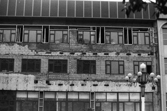 NEOPAN SS 100 (FF)

Image 3 — English Alt Text
A black‑and‑white photo of a multi‑story brick and concrete building showing visible wear and partial disrepair. Some sections of the facade are missing or damaged, exposing bricks and unfinished surfaces. Several windows lack glass panes or frames. In front of the building stands a decorative street lamp with multiple globe‑shaped lights. The image conveys an urban environment with signs of aging architecture.
Image 3 — 中文替代文字
一张黑白照片，画面是一栋多层砖混建筑，外…