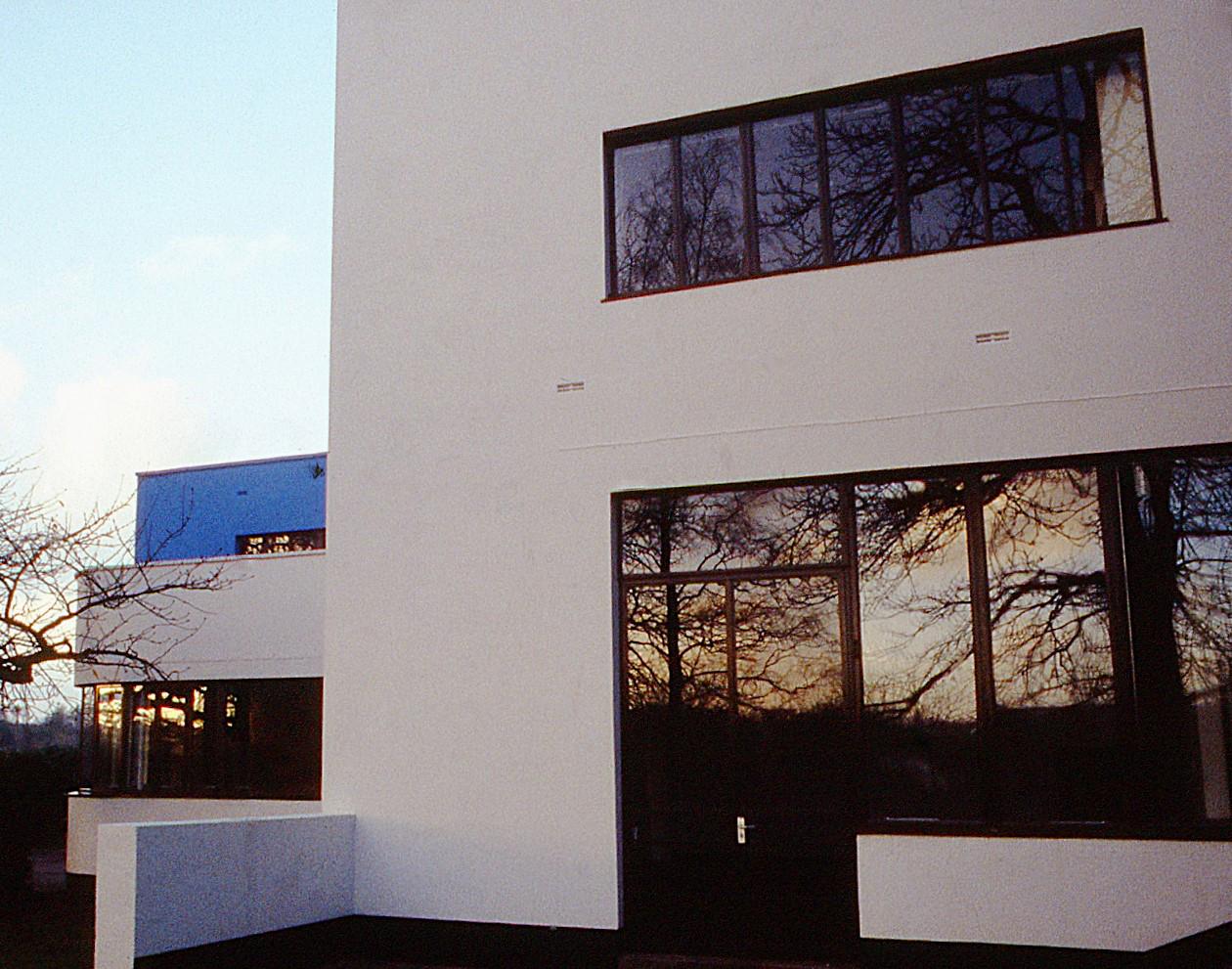 A white, modernist building, with bare trees and a winter sunset reflected in its windows.