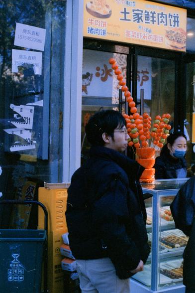 Harman Phoenix 200 II (FF)

English Alt Text
A street food stall displays a bright sign in Chinese listing different meat patties, including beef, pork, and a lettuce‑shrimp‑egg variety. Skewers of glossy candied fruit stand upright in a decorative arrangement. A customer wearing glasses stands in front of the stall, while a masked vendor works behind the counter. Various skewered foods are laid out, and rental signs with a phone number appear on the glass nearby. A green waste‑sorting bin is a…