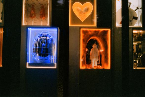 Harman Phoenix 200 II (FF)

English Alt Text:
A wall of six illuminated display windows arranged in a grid. Top left: mannequins in red garments against a brick backdrop. Top center: mannequin head framed by an orange glowing heart with ruffled fabric. Top right: circular satellite-like object. Bottom left: mannequin beside a blue-lit egg-shaped grid. Bottom center: mannequin in white inside an orange tunnel-like space. Bottom right: mechanical components. The vibrant colors and eclectic themes…
