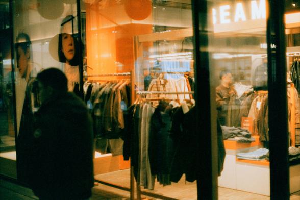 Harman Phoenix 200 II (FF)

English Alt Text
A view through large glass windows into a brightly lit clothing store. Inside, rows of jackets and coats hang neatly on racks, with warm orange lighting throughout the space. A person stands among the racks, appearing to browse or organize clothing. On the left side, a large poster shows several faces, likely models. Outside the store, a person walks past, silhouetted against the bright interior.
Chinese Alt Text（中文替代文字）
透过大玻璃窗看到一家灯光明亮的服装店。店内整齐排列着许多外…