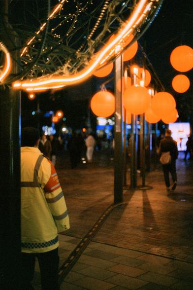 Harman Phoenix 200 II (FF)

English Alt Text
A nighttime pedestrian walkway decorated with large glowing orange spherical lights hanging overhead. A person in a yellow jacket with reflective stripes stands in the foreground facing away. Several people walk in the background. Metal framework and string lights create a festive atmosphere.
Chinese Alt Text（中文替代文字）
夜间的步行通道上方悬挂着许多发光的橙色球形灯，营造出明亮的氛围。前景中，一名穿着黄色反光条夹克的人背对镜头站立。背景中有几位行人经过。金属结构和串灯让场景显得充满节日气氛。