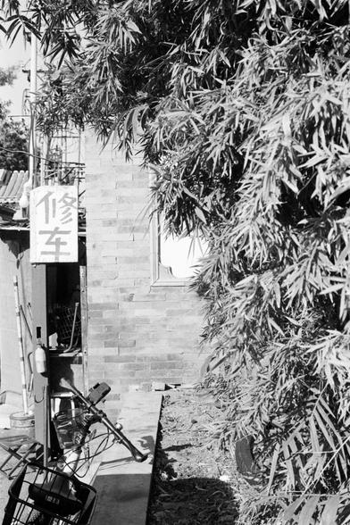 Rollei RPX 400 (FF)
English Alt Text
A black‑and‑white photograph of a small repair shop tucked into a narrow alley. A leafy tree partially hides the shop entrance. A bicycle with a front basket is parked outside, and various tools and items are visible inside the dim shop. The building has a brick wall and a window with a decorative frame. A sign with Chinese characters meaning “vehicle repair” hangs at the entrance.
Chinese Alt Text
一张黑白照片，展示一间位于狭窄巷子里的小修理铺。茂密的树叶部分遮住店门口。店外停着一辆带前篮的自行车，店内昏暗处可见一些…