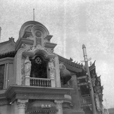 Ilford HP5 Plus 400 (6x6)

English Alt Text
A black‑and‑white photograph of an ornate building combining Chinese and Western architectural styles. The entrance is framed by carved columns and arches, and two statues stand on a balcony above it. The roof has traditional Chinese tiles and decorative ridges. Chinese characters above the entrance and balcony indicate themes related to theater or drama.
中文替代文字
一张黑白照片，展示一座融合中式与西式元素的华丽建筑。入口由雕刻柱子和拱门围成，上方阳台上立着两尊雕像。屋顶为传统中式瓦片和装饰脊。入口和阳台处的中文文字与戏剧相关。