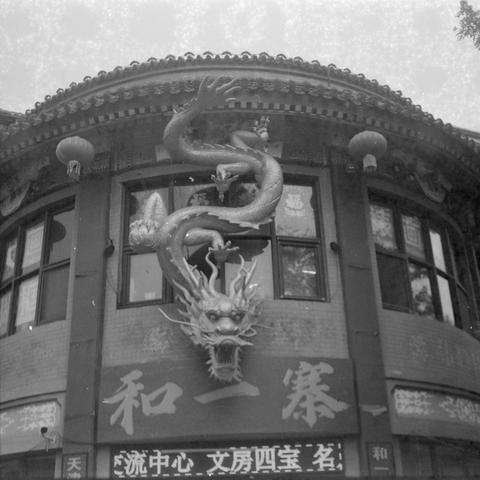 Ilford HP5 Plus 400 (6x6)

English Alt Text
A traditional Chinese-style building with a large, detailed dragon sculpture mounted above the entrance. The dragon appears to leap outward with its mouth open and claws extended. The building has curved roof tiles, hanging lanterns, and ornate wooden details. Chinese characters are displayed on signs near the entrance.
中文替代文字
一座传统中式建筑，入口上方有一条雕刻精细的大龙，张口伸爪，仿佛从屋檐跃出。屋顶是弯曲瓦片，门口挂着灯笼，木雕装饰繁复。入口处的牌匾和窗上可见中文文字。