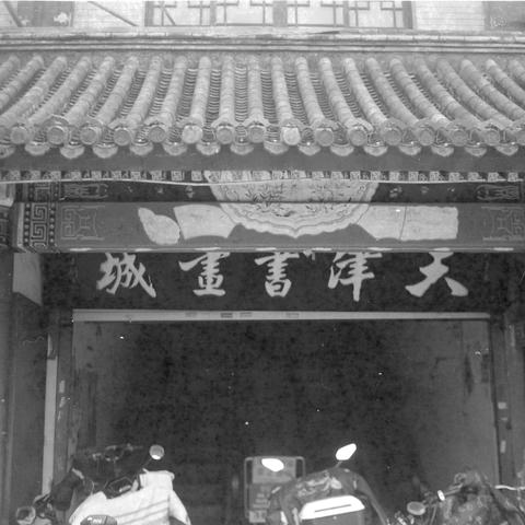 Ilford HP5 Plus 400 (6x6)

English alt text:
A black‑and‑white photograph of the entrance to a traditional Chinese building with an ornate tiled roof and decorative painted beams. A signboard with Chinese characters hangs above the doorway. Several motorbikes are parked in front, blending traditional architecture with modern urban life.
中文替代文字：
一张黑白照片，展示一座传统中式建筑的入口，屋顶为精致的瓦片结构，梁柱上有装饰性彩绘。门上方悬挂着写有中文的匾额。入口前停放着多辆摩托车，呈现传统建筑与现代城市生活的交织。