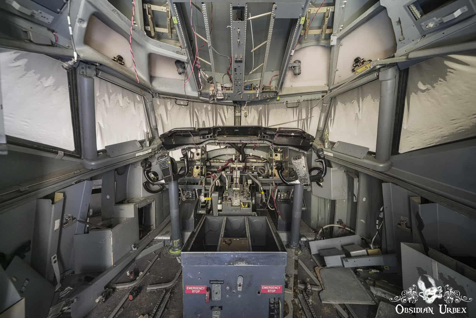 An abandoned Boeing 737 flight simulator cockpit appears stripped, with exposed wiring and missing panels.