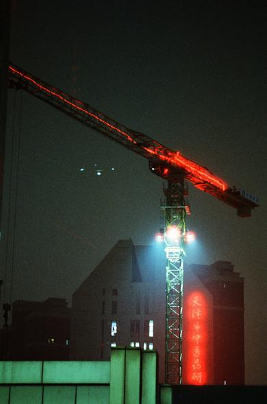 CineStill 800T (FF)

English Alt Text
A nighttime city scene featuring a tall construction crane lit with red lights along its arm and bright white lights at its base. The crane rises against a dark sky, with several mid‑rise buildings behind it. One building displays a vertical red neon sign with Chinese characters. The overall atmosphere is dramatic, with strong contrasts between the artificial lights and the surrounding darkness.
中文替代文字
夜间城市景象，一座高大的施工起重机矗立在黑暗的天空前。起重机的臂架上有红色灯光，底部有明亮的白光。背景中有几栋…