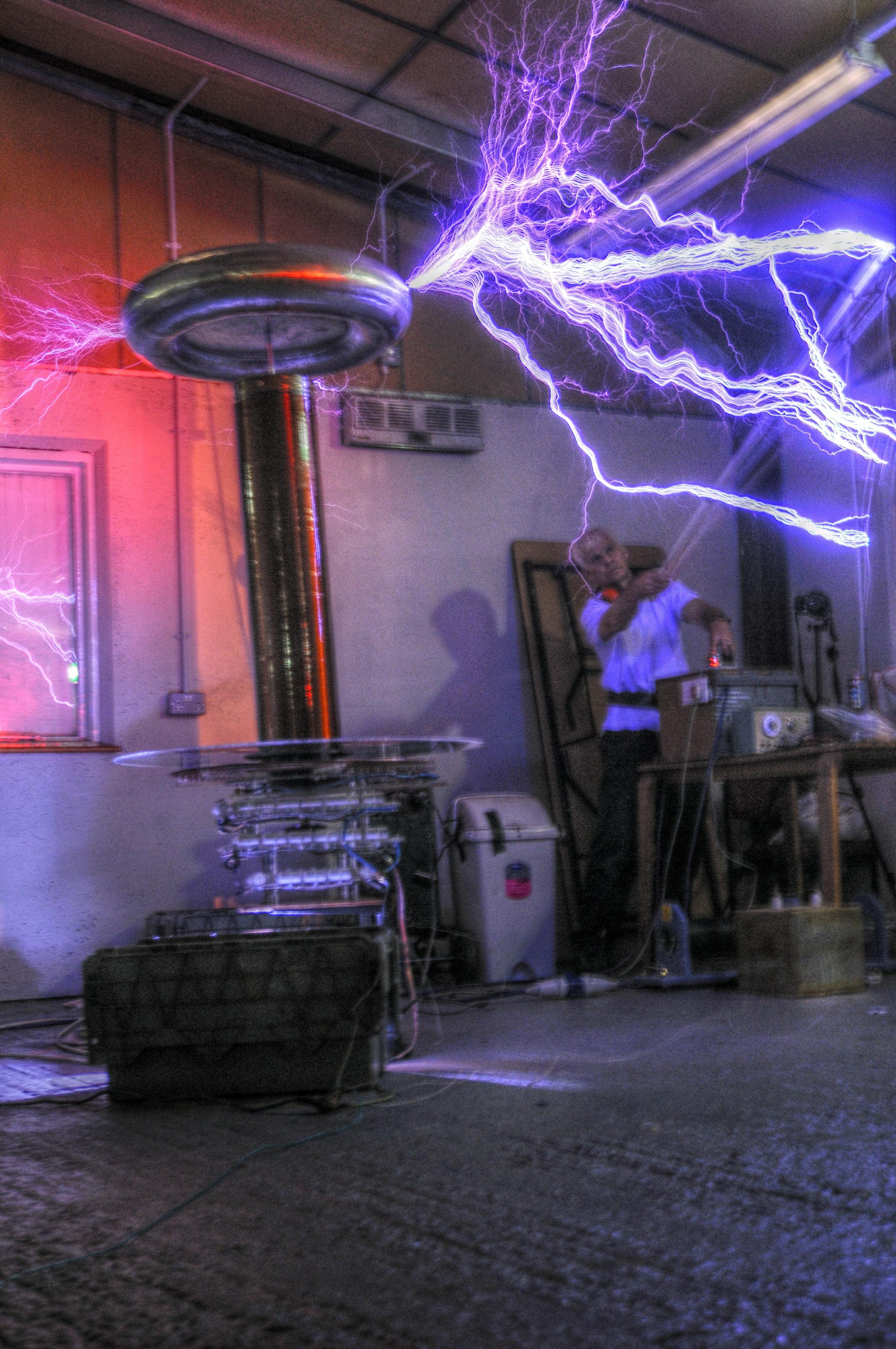 Tesla coil with large electrical discharges and a man with a chicken stick drawing arcs from it. #gaussfest
