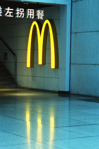 CineStill 800T (FF)

English Alt Text
An indoor area featuring a large illuminated McDonald’s golden‑arches logo mounted on a wall. The bright yellow “M” reflects clearly on the shiny tiled floor. Above the logo is Chinese text. To the left, a staircase leads upward, suggesting the space is part of a larger building such as a mall or transit hub. The lighting is warm and highlights the contrast between the sign and the surrounding interior.
中文替代文字
室内空间中，一面墙上悬挂着明亮的麦当劳金色拱门标志，黄色“M”字在光亮的瓷砖地面上形成清晰倒影…