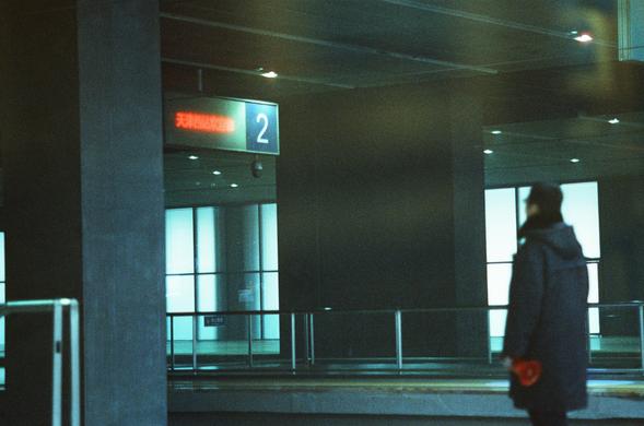CineStill 800T (FF)

English Alt Text
A person in a dark coat stands inside a transportation terminal with large glass windows and tall structural columns. They hold a red object in their hands. A digital sign above displays red Chinese text reading “Welcome to Tianjin West Station.” A blue sign with the number “2” hangs nearby, and a smaller sign in the background reads “P2 Exit.” The lighting is dim, creating a calm, waiting‑area atmosphere.
中文替代文字
一名穿深色外套的人站在交通枢纽大厅内，周围是大型玻璃窗和高大的结构柱。他手中拿着一个红色…