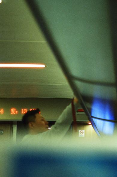 CineStill 800T (FF)

English Alt Text
The interior of a train or subway car with soft, dim lighting. A person reaches upward toward an overhead compartment or rail, though the image is slightly out of focus. A digital display in the background shows red Chinese characters and the number “13,” possibly indicating temperature or time. A “No Smoking” sign with Chinese text is mounted on the wall behind the person. The scene captures a quiet moment during transit.
中文替代文字
一节列车或地铁车厢内部，灯光柔和偏暗。画面略微模糊，一…