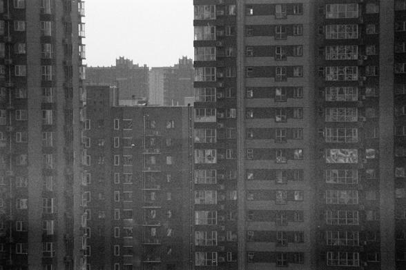 Ilford HP5 Plus 400 (FF)

English alt text:
A black‑and‑white view of several tall apartment buildings standing very close together. Each building has rows of identical windows and balconies, some with air‑conditioning units attached. The structures fill the frame tightly, creating a sense of repetition and density. No people are visible. The overall atmosphere feels crowded and urban, with strong contrasts between light and shadow on the building facades.
中文替代文字：
一幅黑白城市景象，画面中多栋高耸的住宅大楼紧密排列。楼面上布…
