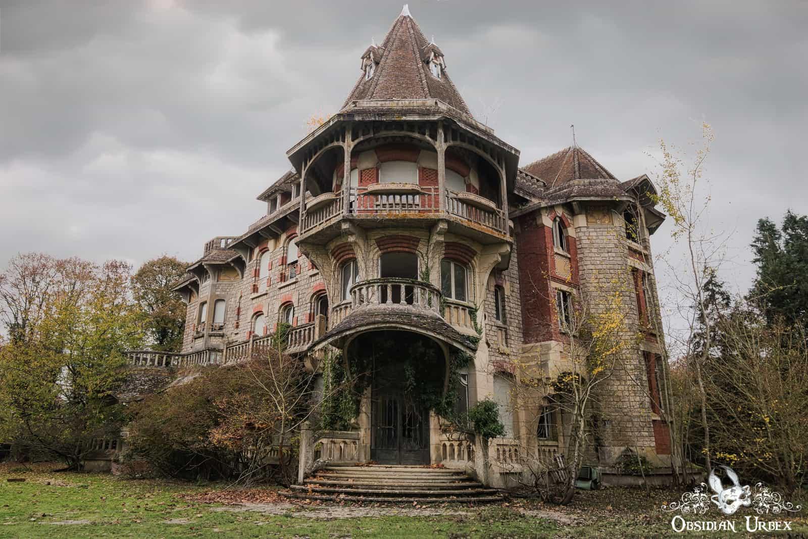 An abandoned French chateau with a striking central tower, ornate balconies, and an ivy-draped entrance.