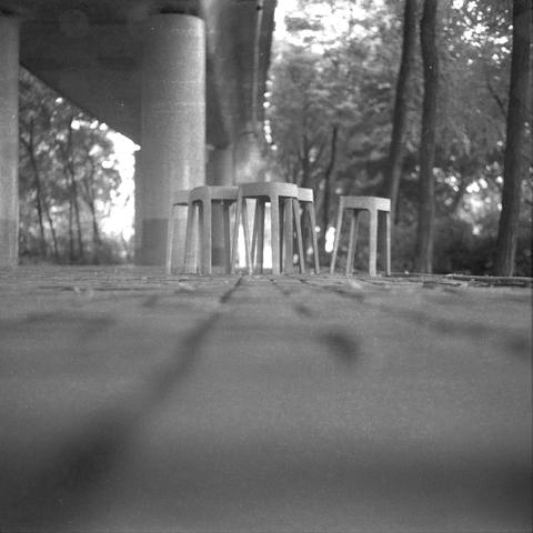 Ilford HP5 Plus 400 (6x6)

English Alt Text

A black‑and‑white low‑angle photo showing plastic stools on a paved surface beneath a large elevated structure. Tall trees stand in the background, and sunlight filters through the leaves. The perspective emphasizes the ground texture and the vertical lines of the stools and columns. The scene feels quiet and outdoors.

Chinese Alt Text

一张黑白低角度照片，画面中塑料小凳子摆放在铺装地面上，上方是大型高架结构。背景有高大的树木，阳光从树叶间洒下。视角突出地面纹理以及凳子和柱子的垂直线条。整体氛围安静，位于户外。