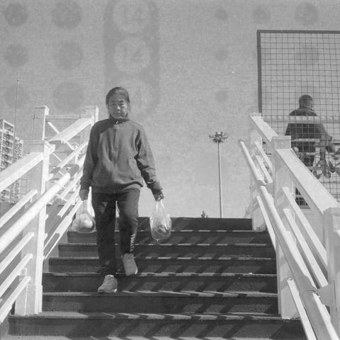 Ilford HP5 Plus 400 (6x6)

English Alt Text

A black‑and‑white photo of a person walking down outdoor stairs while holding plastic bags in both hands. The person wears casual clothing, including a zip‑up jacket and sneakers. Another person is visible behind a metal fence on the opposite staircase. Buildings and a tall light pole appear in the distance. The image has a textured, film‑like surface.

Chinese Alt Text

一张黑白照片，一名手提塑料袋的人正走下户外楼梯，穿着休闲外套和运动鞋。另一侧楼梯上、金属栅栏后可见另一名行人。远处有建筑物和高灯杆。画面带有胶片质感的纹理。