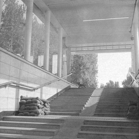 Ilford HP5 Plus 400 (6x6)
English alt text

A black‑and‑white photo of a stairway leading upward toward an outdoor area with trees. The stairway is enclosed by tiled walls and has metal handrails on both sides. Several sandbags are stacked along the base of both walls. At the top of the stairs, part of a bicycle is visible leaning against a wall. The ceiling above the stairs has a slatted pattern with a light fixture. The overall scene appears functional and urban, with no people present.

中文替代…