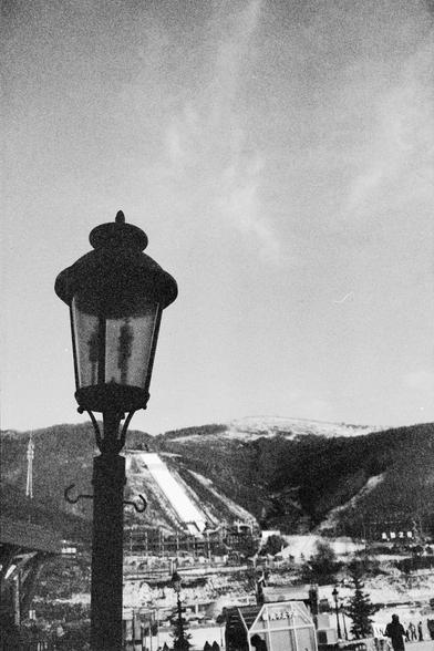 Ilford FP4 Plus 125 (FF)

English alt text
A black‑and‑white photograph featuring a tall streetlamp in the foreground. Behind it, a large ski‑jump ramp extends down a snowy hillside. Several small buildings and people are visible at the base of the ramp, indicating an active winter sports area. The contrast between the dark lamp silhouette and the bright snow makes the ramp stand out clearly.
中文替代文字
一张黑白照片，前景是一盏高大的街灯。背景中，一座大型跳台滑雪坡道沿着积雪的山坡延伸。坡道底部有一些建筑物和行人，显示这里是冬季运动场地。街灯的深色轮廓与明亮的雪面形成对比，使跳台格外醒目。