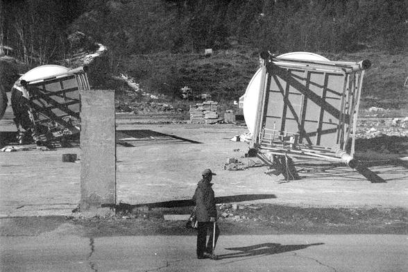 Ilford FP4 Plus 125 (FF)

English alt text
A black‑and‑white image of a person standing outdoors near two large cylindrical structures lying on their sides. The structures have visible metal frameworks and appear to be industrial tanks or containers. A tall concrete pillar partially blocks the view of one cylinder. The person is wearing a coat and hat and holding an umbrella, facing the structures. Behind them is a forested hillside. The scene suggests an industrial or construction area.
中文替代文字…