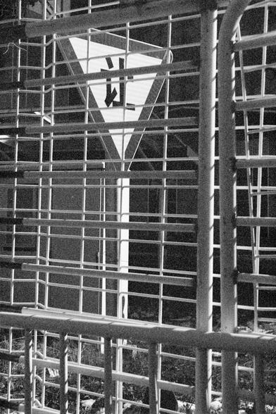 Ilford FP4 Plus 125 (FF)

mage 3 – English Alt Text
A nighttime black‑and‑white image showing a triangular traffic sign behind a metal fence. The sign is illuminated and displays the character “让,” meaning “give way to.” Vertical and horizontal metal bars in the foreground partially obscure the sign, creating a grid‑like pattern. The background is dark, making the lit sign stand out.
Image 3 – 中文替代文字
一张黑白的夜间照片。画面中，一个三角形交通标志位于金属栅栏后方，标志被照亮，上面有“让”字。前景的金属栏杆形成网格状，部分遮挡了标志。背景较暗，使得被照亮的标志更加突出。