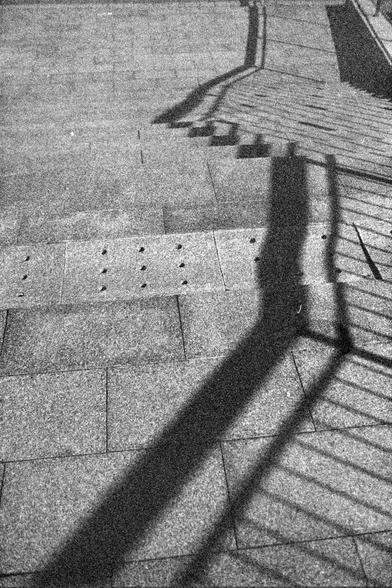 Ilford FP4 Plus 125 (FF)

English alt text
A black‑and‑white photo of outdoor steps made of stone or concrete. A metal railing runs along the side, casting long, parallel shadows across the steps. At the top of the stairs is a section of tactile paving with raised dots. The image highlights the contrast between light and shadow.
中文替代文字
一张黑白照片，画面为户外的石质或混凝土台阶。旁边的金属扶手在台阶上投下平行的长影。台阶顶部有一块带凸点的盲道铺面。画面强调光影之间的对比。