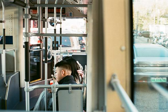 Lucky  C200 (FF)
English:

The interior of a bus, viewed from the back. Two passengers are seated near the front: one man is looking outside, and a woman next to him looking at her phone. The bus is in motion, and the street scene outside is slightly blurred. The bus has metal handrails and a digital display above the front door.
Chinese:

从公交车后部拍摄的车内景象。两名乘客坐在前排：一名男子看着前方，旁边的女子看着她的手机。公交车正在行驶，车窗外的街景略显模糊。车内有金属扶手，前门上方有电子显示屏。