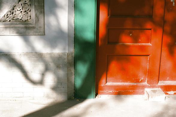 Lucky  C200 (FF)

- **English:** A close-up of a red door with green framing, set in a grey brick wall. Sunlight casts shadows of tree branches on the door and wall.
- **中文:** 灰色砖墙上的一扇红色门，门框为绿色。树枝的影子投射在门和墙上。