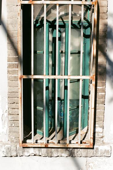 Lucky  C200 (FF)

- **English:** A window with rusted metal bars and turquoise window frames, set in a grey brick wall. The window appears to be slightly ajar.
- **中文:** 灰色砖墙上的一扇带铁锈金属栏杆的窗户，窗框为青绿色，窗户微开。