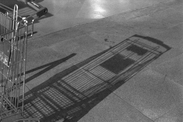 Ilford FP4 Plus 125 (FF)

English:
A black-and-white photograph of a shopping cart on a paved surface. The cart casts a long, detailed shadow on the ground, highlighting the texture of the pavement.

Mandarin Chinese:
一张黑白照片，展示了一个购物车停在铺砌的地面上。购物车在地面上投下长长的、细节丰富的阴影，突出了地面的纹理。