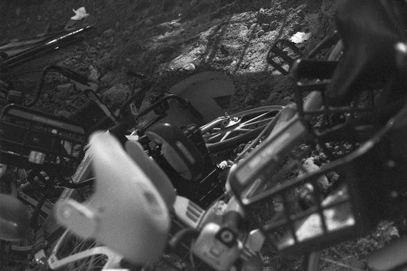 Ilford FP4 Plus 125 (FF)

English: A black-and-white close-up of a damaged bicycle lying on its side on a dirt or gravel surface. The bicycle's parts, such as the handlebars and engine, are visible and appear to be broken or dislodged.
中文: 一张黑白照片，近距离拍摄了一辆侧翻在地的自行车，地面是泥土或砾石。车的部件，如车把和引擎，看起来损坏或脱落。