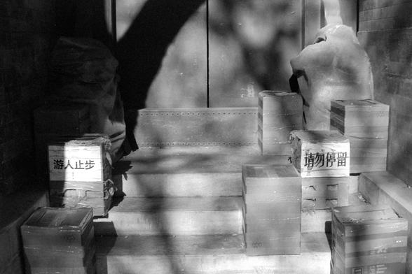 Ilford FP4 Plus 125 (FF)

English:
A black-and-white photograph showing a stack of cardboard boxes, some of which are labeled. The box on the left has Chinese characters that read "游人止步" (No entry for visitors). The box on the right has Chinese characters that read "请勿停留" (No stopping). The boxes are piled up in a somewhat disorganized manner, with a person partially visible in the background, appearing blurred.

中文：
一张黑白照片，展示了一堆纸箱，部分纸箱上有标签。左边的纸箱上写着“游人止步”几个字，右边的纸箱上写着“请勿停留”。纸箱堆放得有些杂乱，背景中有一个模糊的人影。
