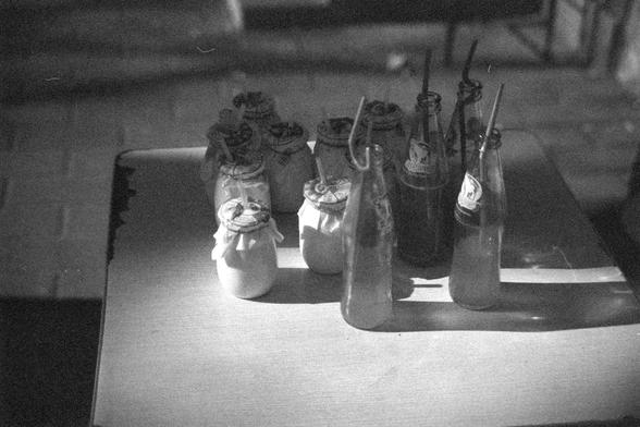 Ilford FP4 Plus 125 (FF)

##English
A black-and-white photograph of several glass bottles placed on a windowsill or table. Some bottles are covered with cloth or paper, and a few have straws inserted. The bottles are arranged in a row, and light is shining through them, creating shadows on the surface.

##中文
一张黑白照片，照片中几个玻璃瓶放在窗台或桌子上。有些瓶子用布或纸包着，几个瓶子里插着吸管。瓶子排成一排，光线穿过瓶子，在地面上投下影子。