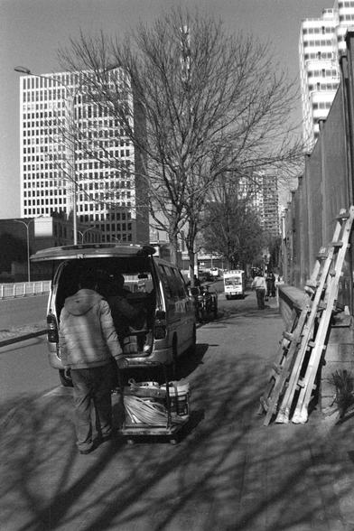 Ilford FP4 Plus 125 (FF)

##English

A black-and-white street scene featuring a person unloading or organizing items from the back of a van. The van is parked along a sidewalk lined with tall buildings in the background. A ladder is leaning against a wall on the right side of the image.

##中文

一张黑白街景照片，照片中一人正从一辆面包车后备箱卸货或整理物品。面包车停靠在人行道旁，背景是高楼林立的街道。图片右侧有一架梯子靠在墙上。