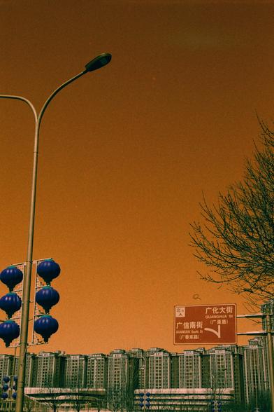 Harman Switch Azure (FF)

English

A city street at dusk, with a street sign in both Chinese and English reading "Guanghua St" and "Guangxin South St." The sky is orange, indicating sunset or heavy pollution. A row of blue lanterns hangs from a traffic light pole on the left. In the background, there are tall apartment buildings, and a bare tree is visible on the right.

中文

黄昏时分的城市街道，街牌上用中英文标注“光华街”和“广信南街”。天空呈橙色，暗示日落或空气污染严重。左侧交通灯杆上挂着一排蓝色灯笼。背景是高层公寓楼，右侧可见光秃的树木。