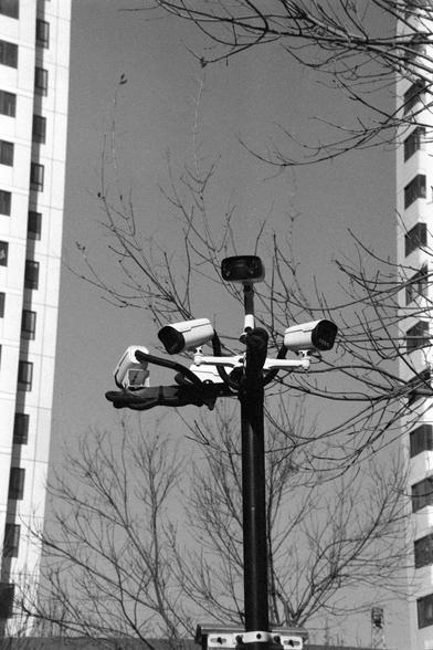 Ilford FP4 Plus 125 (FF)

English

A black-and-white photograph showing a tall pole with multiple surveillance cameras attached to it. The cameras are pointed in different directions. In the background, there is a tall apartment building with many windows and balconies. Leafless tree branches are visible in front of the building.

中文

一张黑白照片，展示了一个高高的杆子，杆子上安装了多个监控摄像头，摄像头指向不同的方向。背景中有一栋高层公寓楼，楼上有许多窗户和阳台。楼前有光秃秃的树枝。