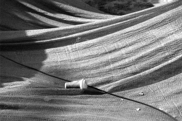 Ilford FP4 Plus 125 (FF)

##English

A black-and-white photograph showing a close-up of a woven mesh or netting material. The mesh is draped in overlapping layers, creating a textured pattern of light and shadow. In the center, a small white paper coffee cup is partially visible, resting on the mesh.

##中文

一张黑白照片，展示了编织网或网状材料的特写。网状物以多层重叠的方式铺开，形成了光影交错的纹理图案。中间有一个小的白色纸质咖啡杯，部分可见，放置在网状物上。