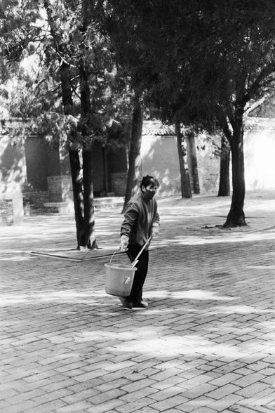 Lucky LUCKY SHD 400 (FF)

##English

A black and white photograph of a person walking outdoors. The person is wearing a jacket, pants, and a face mask, and is carrying a bucket in one hand. The scene is set in a park or courtyard with trees and a paved path. The trees cast shadows on the ground, and the person appears to be walking along the path.

##中文

一张黑白照片，拍摄的是一个在户外行走的人。这个人穿着外套、裤子，戴着口罩，一只手提着一个水桶。场景设在一个公园或庭院，周围有树木和铺砌的小路。树木在地面上投下影子，这个人看起来正沿着小路行走。
