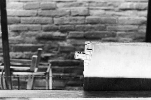 Lucky LUCKY SHD 400 (FF)
##English

A black and white photograph showing a close-up of an object, a file clip on a metal. The background includes a brick wall and a metal railing, with a chair partially visible in the background.

##中文

一张黑白照片，特写拍摄的是一个白色物体，一个夹在金属上的夹子。背景中有一面砖墙和一个金属栏杆，还有一把椅子部分可见。