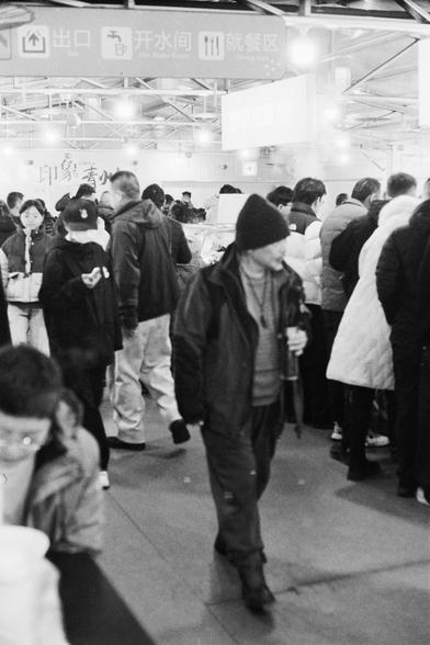Lucky LUCKY SHD 400 (FF)

##English

A black-and-white photograph of a crowded indoor space. People are standing and walking, some carrying luggage. Overhead signs in Chinese indicate directions for exits, restrooms, and ticket areas. The atmosphere is busy, with many individuals dressed in winter clothing.

##中文

一张黑白照片，展示了一个拥挤的室内空间。人们站着或行走，有些拖着行李。头顶上的中文标志指示出口、洗手间和售票区的方向。现场气氛繁忙，很多人穿着冬季服装。
